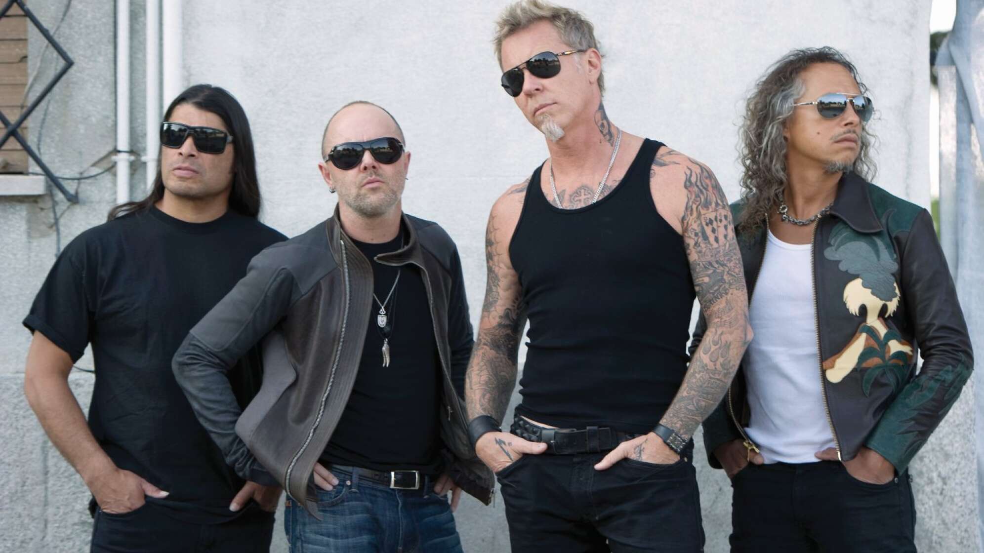 Metallica posieren nebeneinander vor einer weißen Hauswand
