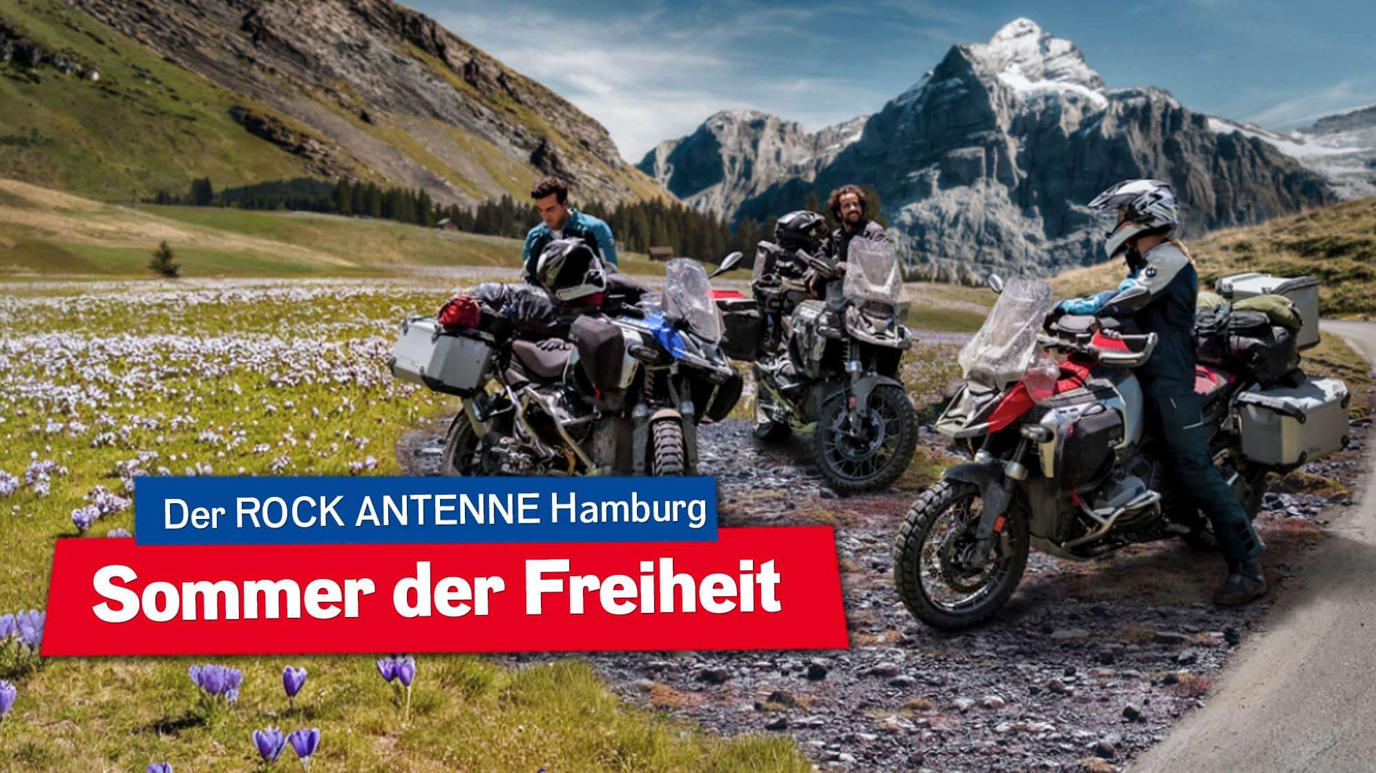 Drei Motorradfahrer machen Rast auf einem Schotterparkplatz in den Bergen, im Hintergrund der Gipfel, im Vordergrund grüne Wiese mit ein paar blühenden Krokussen, die drei Fahrer stehen bei ihren BMW GS Motorrädern und reden, dazu ein Button mit dem Text: Der ROCK ANTENNE Hamburg Sommer der Freiheit
