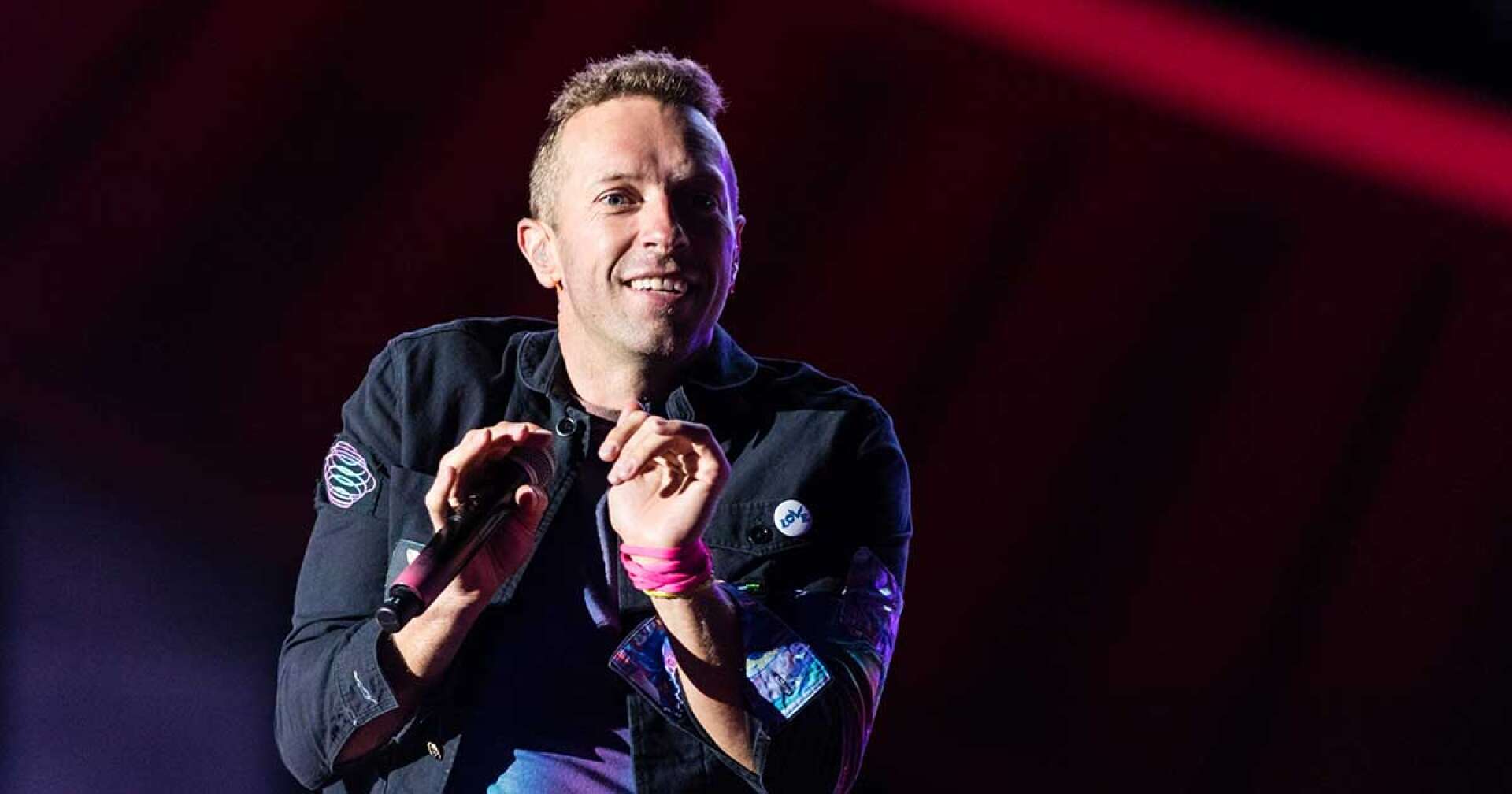Chris Martin von Coldplay lächelnd mit Mikro in der rechten Hand