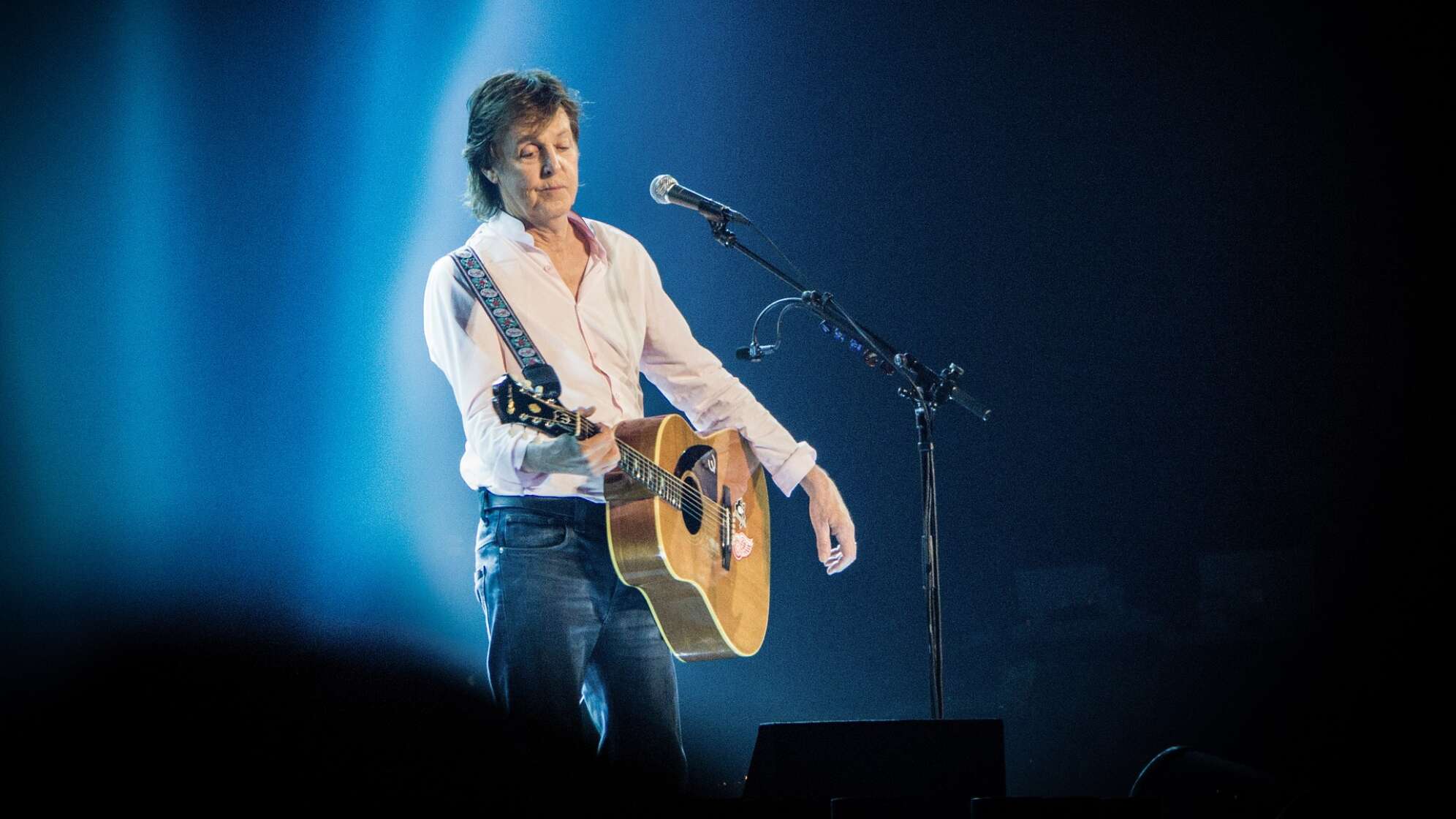 Paul McCartney steht mit seiner Akustik-Gitarre im Scheinwerferlicht
