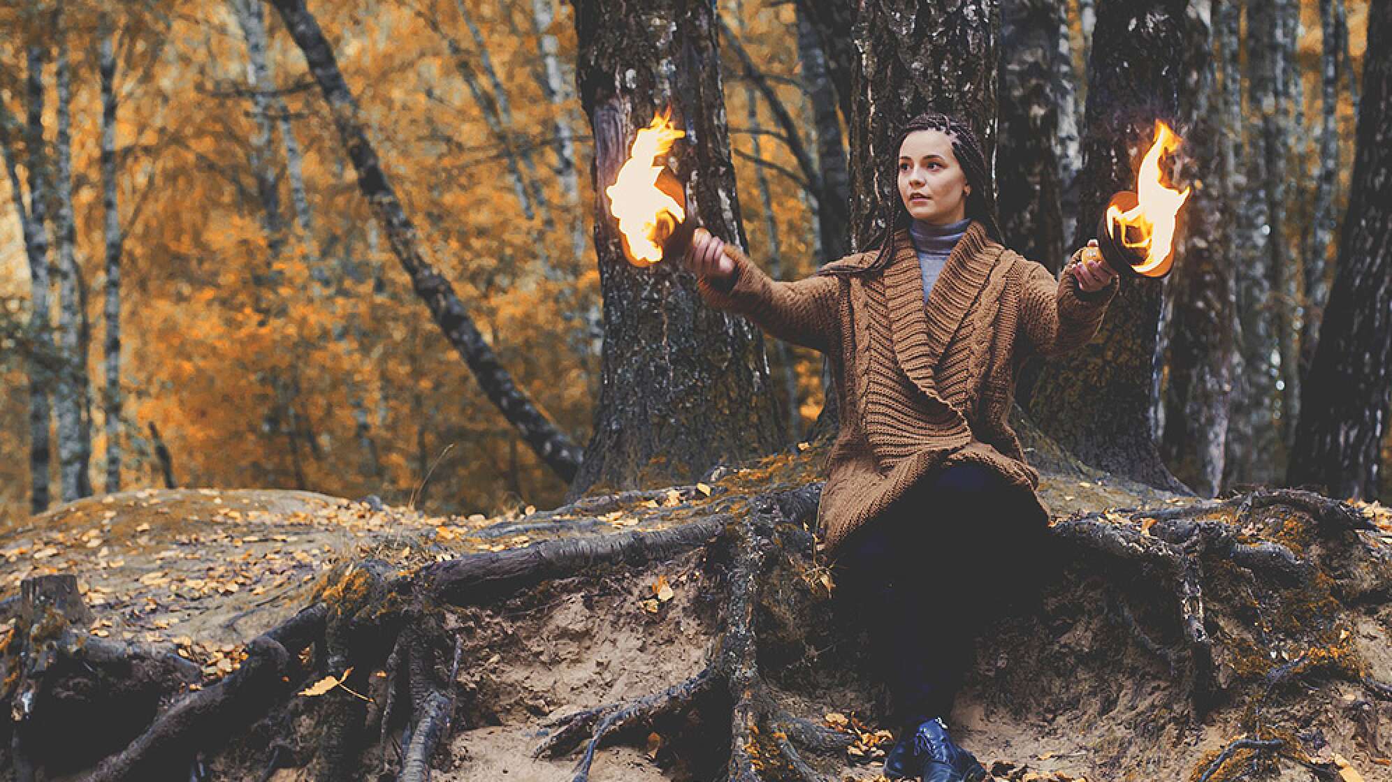 Frau sitzt im Wald mit Feuer in ihren Händen