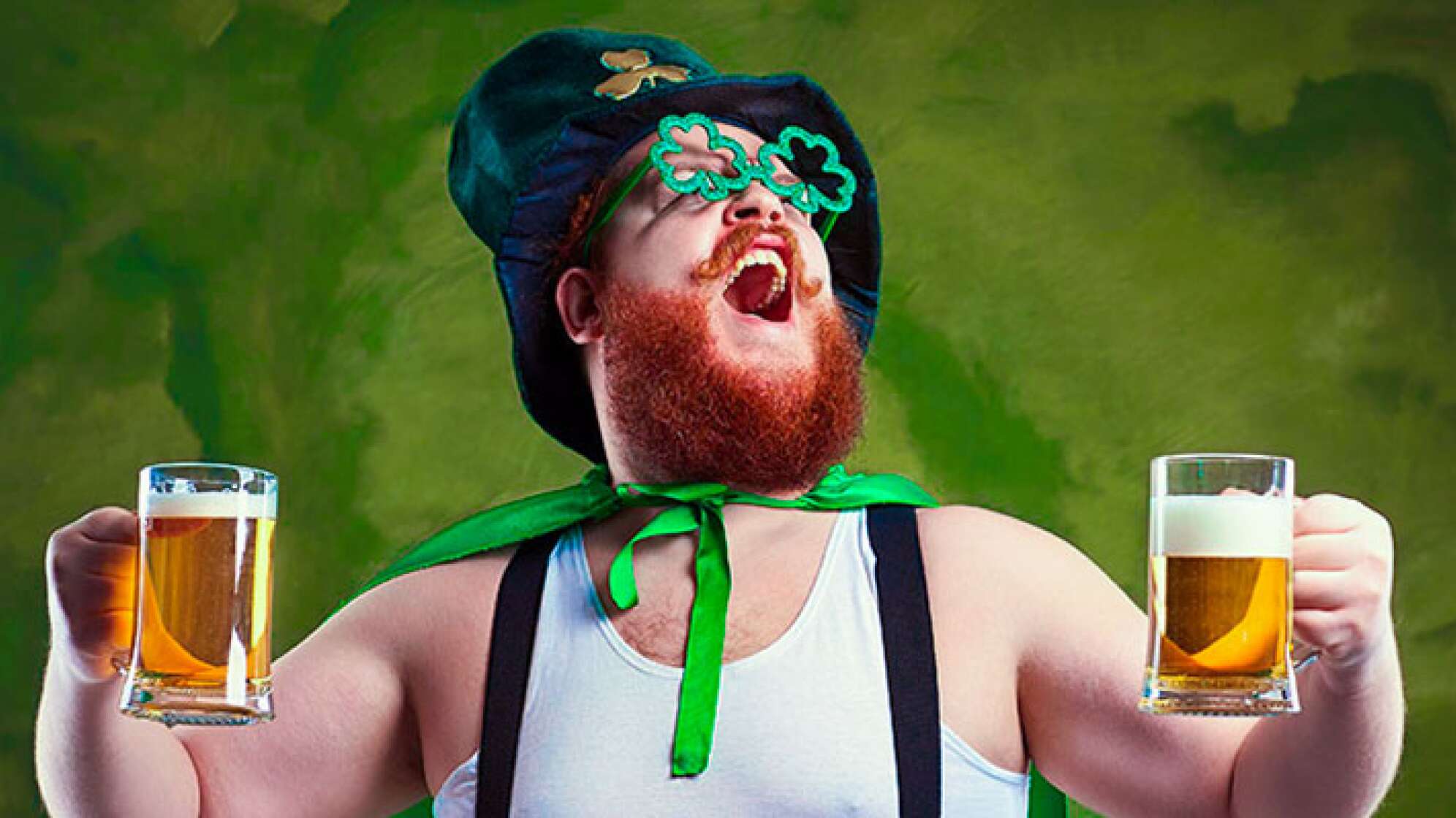A fat man with a beard in St. Patrick's suit is smiling with a mug of beer on a green background.