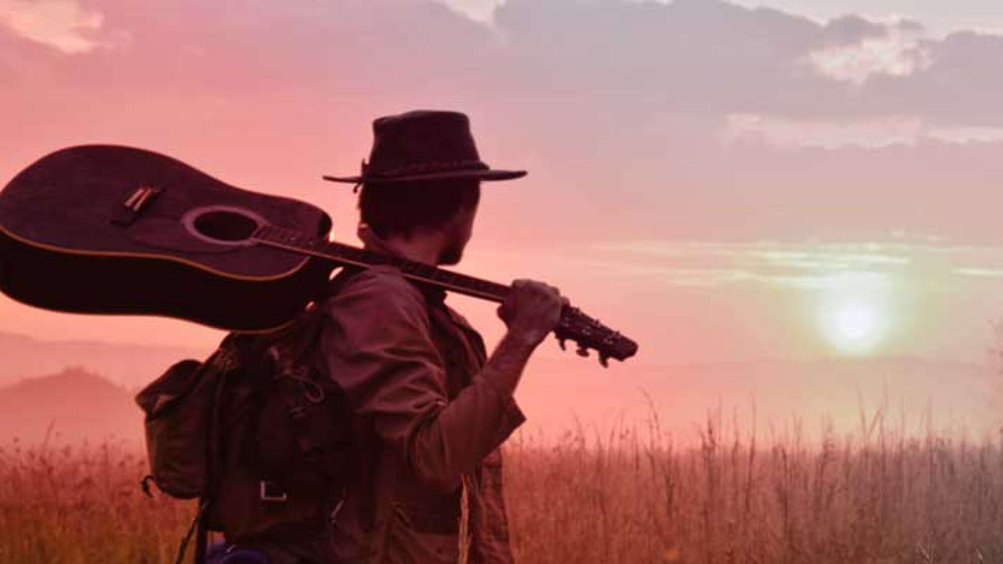 Mann mit Gitarre schaut in einen Sonnenuntergang