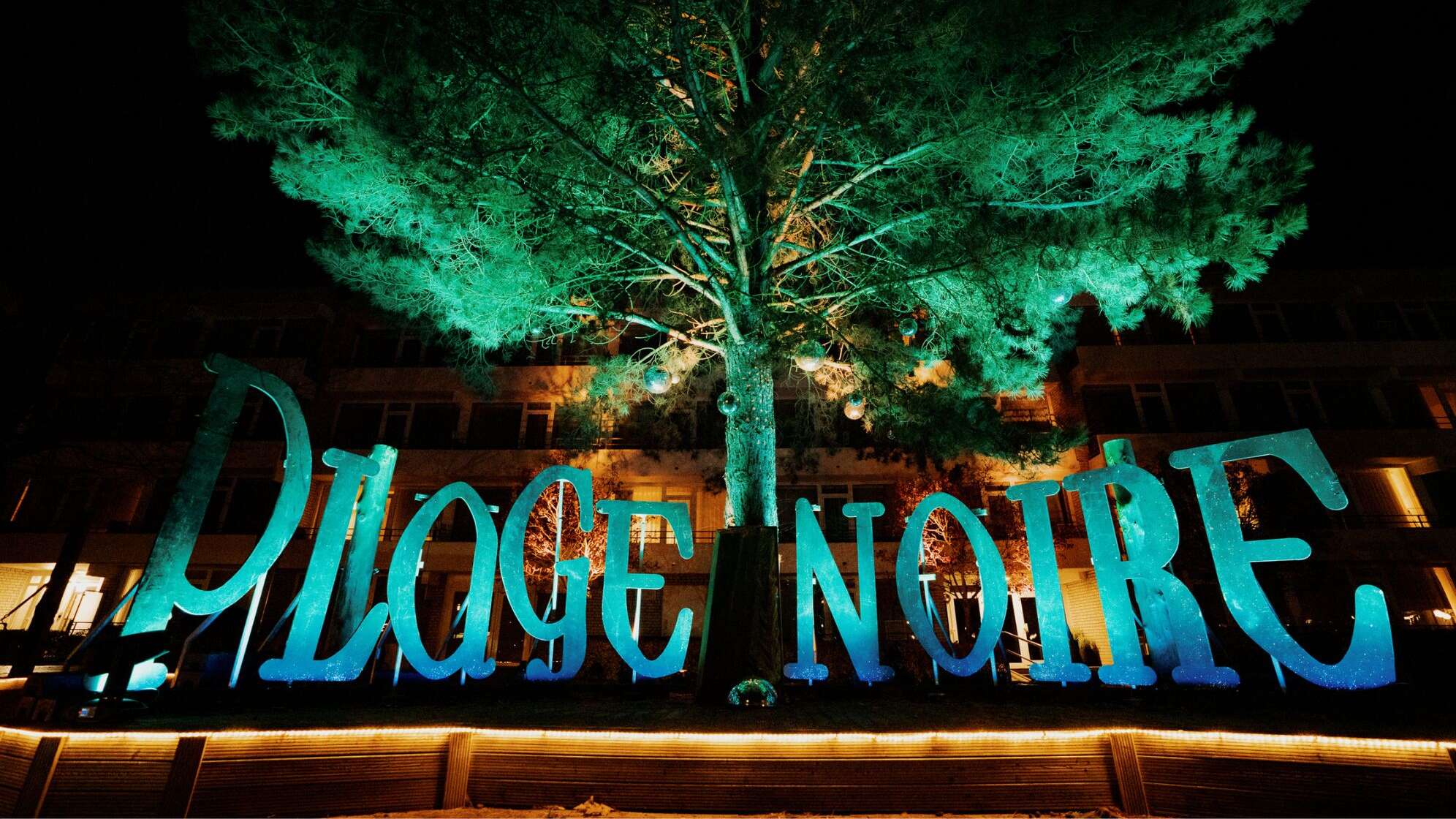 Das Plage Noire in einer aufgestellten Schrift unter einem Baum, Grün und Blau beleuchtet