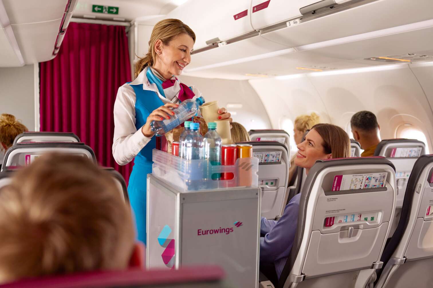 Eine Flugbegleiterin bei Eurowings versorgt Fluggäste mit Erfrischungen und lächelt