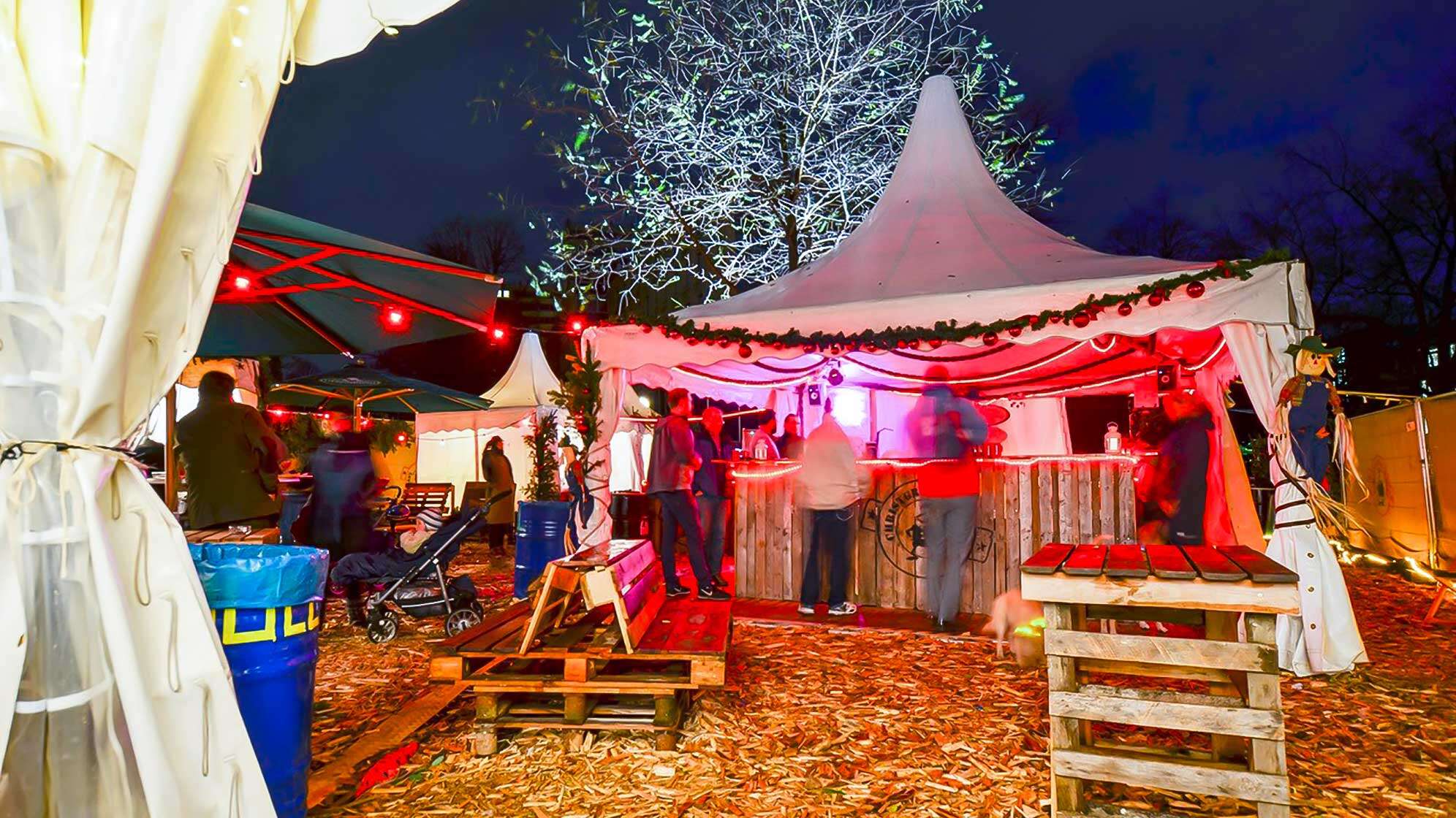 Das Ambiente des Christgrindelmarkts - auf dem Boden liegt Stroh, im Hintergrund steht ein beleuchtetes Zelt, aus dem Glühwein verkauft wird.