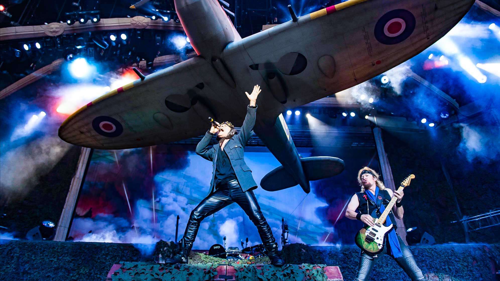 Sänger Bruce Dickinson und Gitarrist Adrian Smith auf der Bühne von Iron Maiden - über ihnen schwebt ein großes Militärflugzeug.