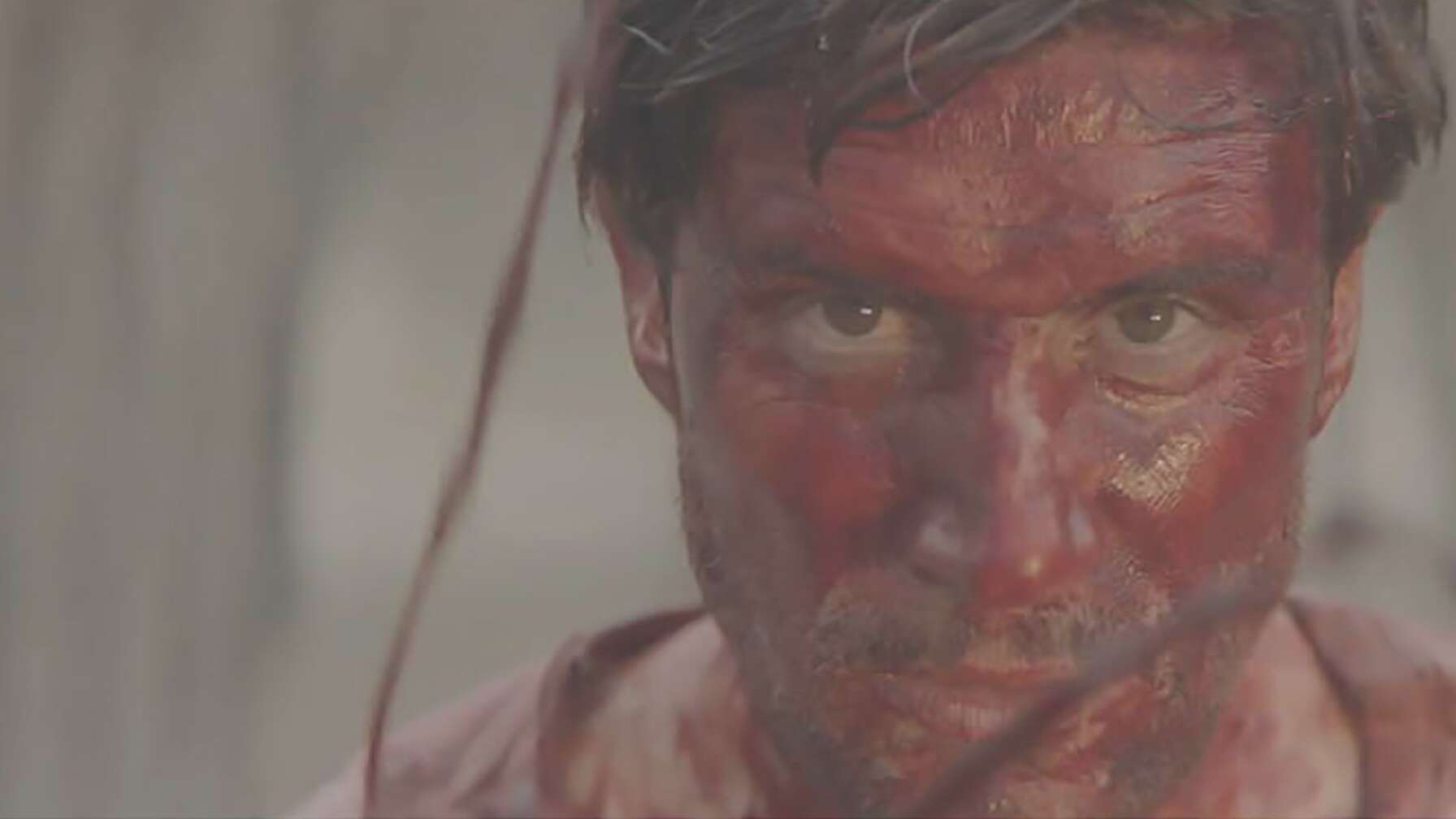 Michael Lombardi in seiner Rolle als John Bishop. Man sieht den Schauspieler mit blutverschmiertem Gesicht.