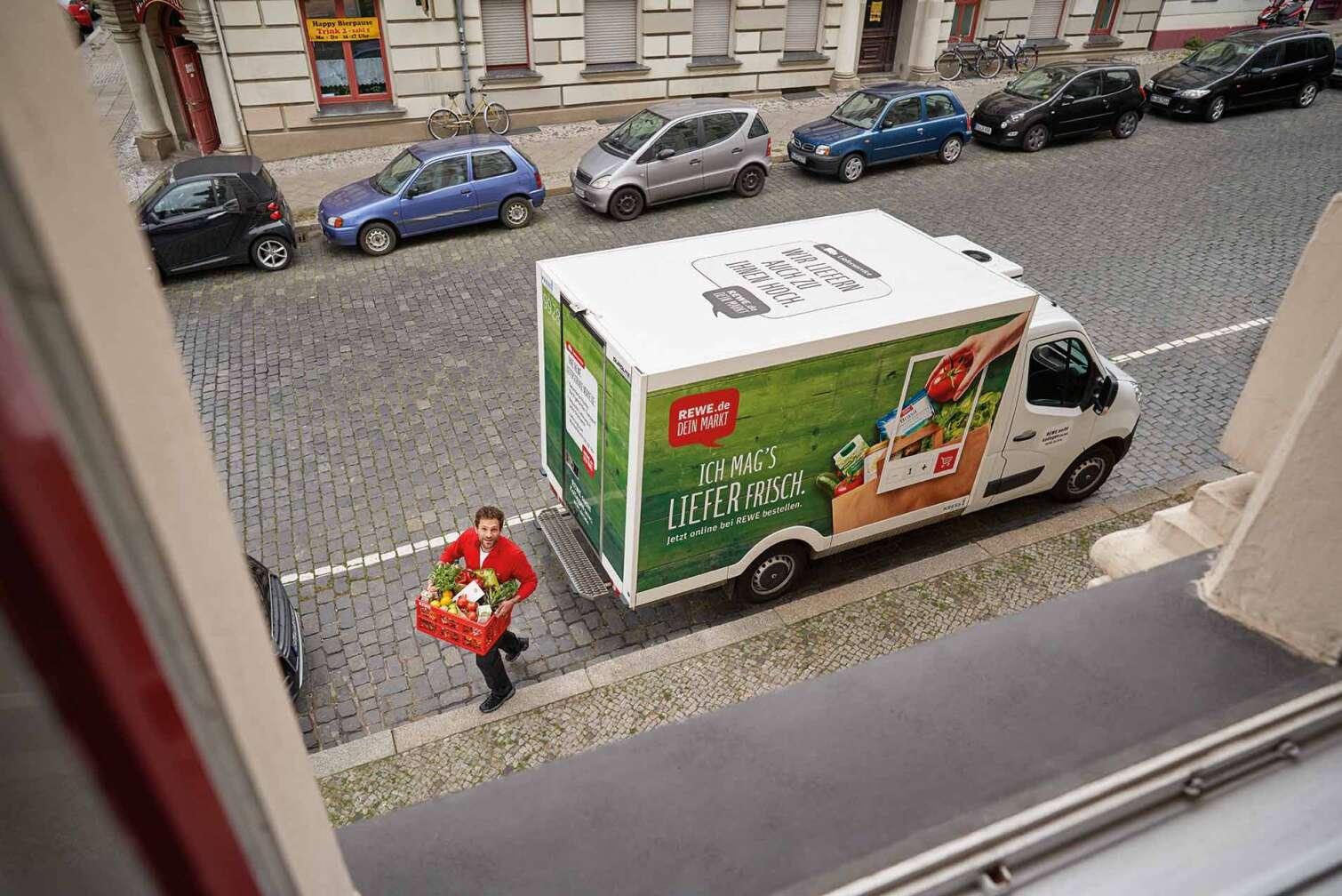 Bild eines REWE Lieferservice LKWs auf der Straße, Blick hinab aus einem Fenster