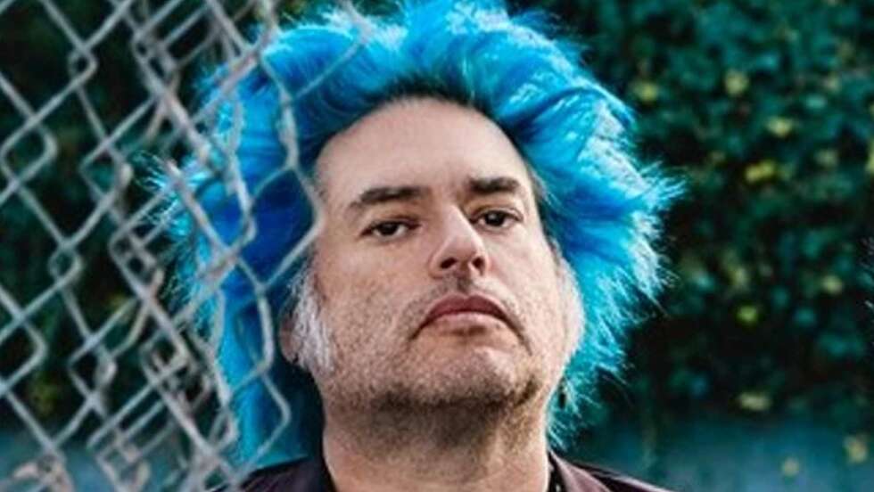Fat Mike von NOFX mit blauen Haaren hinter einem Zaun