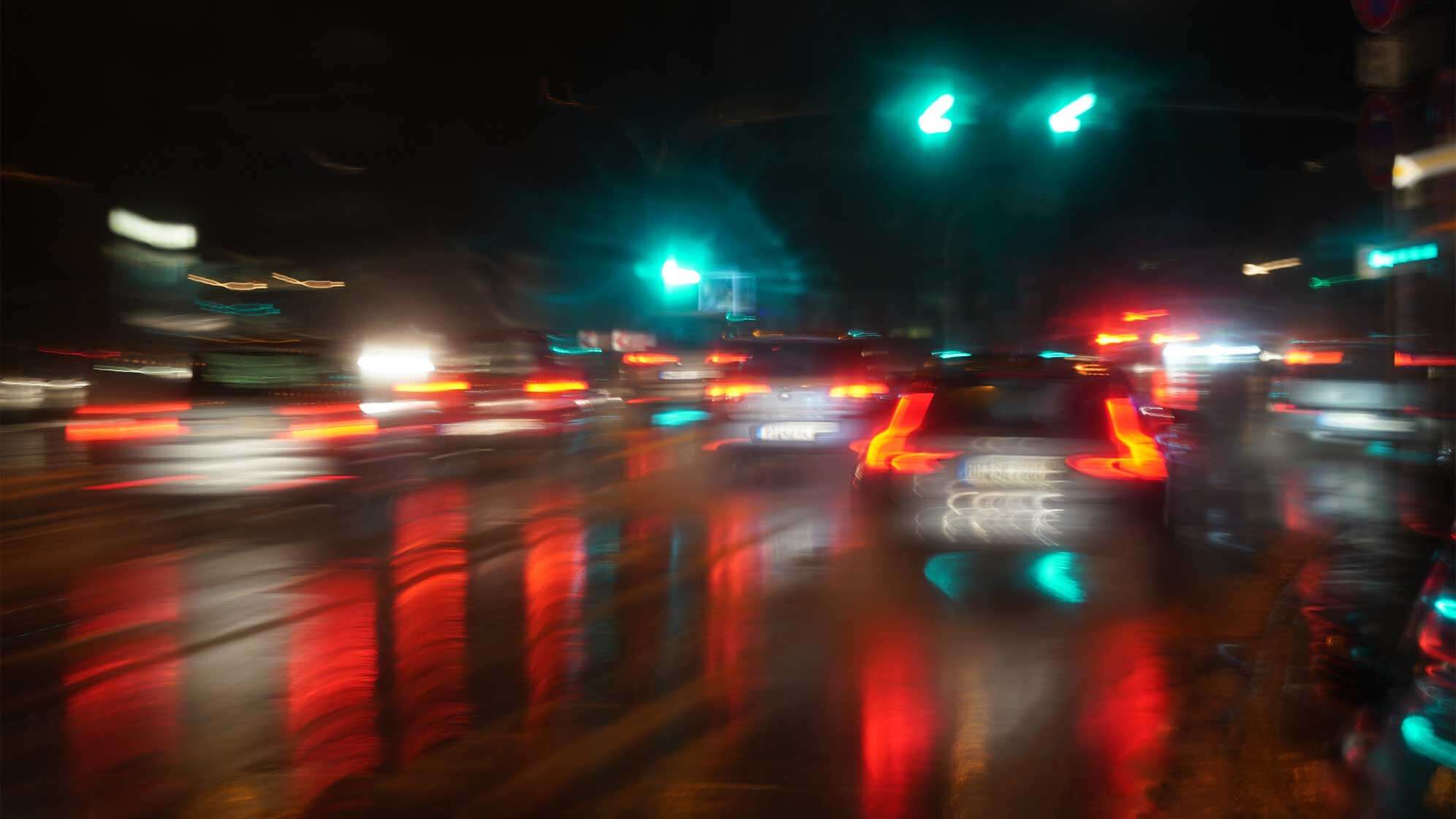 Hamburg: Die Lichter von Ampeln und Fahrzeugen spiegeln sich auf einer regennassen Straße.