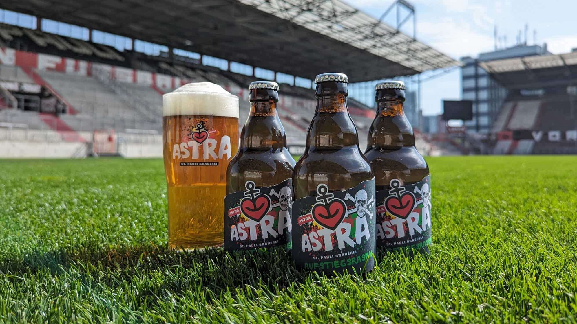 Drei Flaschen und ein volles Bierglas der ASTRA Sonderedition Aufstiegsrasen stehen auf der Rasenfläche im Millerntorstadion