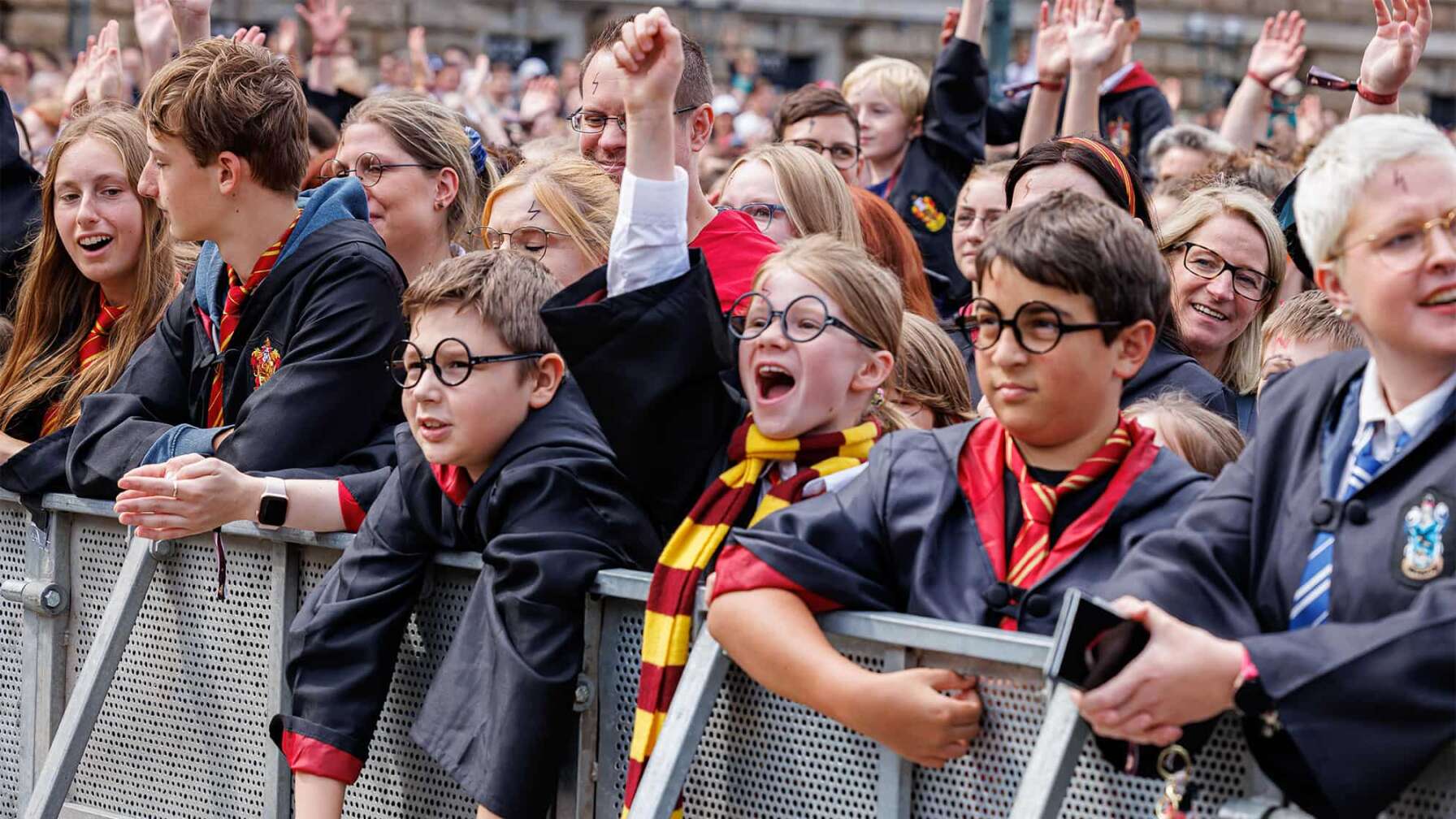 Verkleidete Harry Potter-Fans an einer Absperrung, die jubeln und die Arme heben