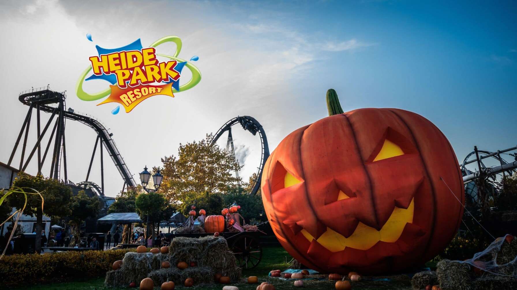 Ein geschnitzes Kürbisgesicht in Großaufnahme vor Achterbahnen des Heide Park Resort im Hintergrund